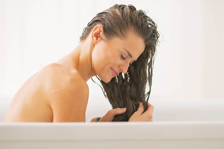 Happy young woman washing hair in bathtub