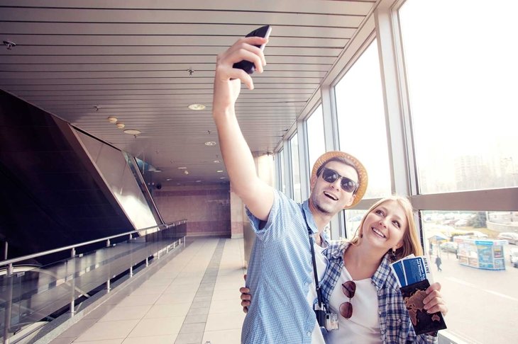We love traveling! Vacation Selfie. Beautiful young loving couple making selfie by their smart phone while waiting for boarding in the airport.