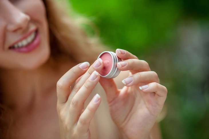 Lip balm. Pretty young woman holding lip balm in her hand and smiling
