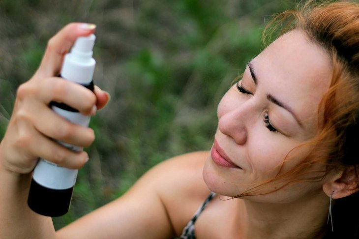 Top view on Girl with a spray bottle in her hands, sprays water on her face. Natural cosmetics, handmade for refreshment in the hot summer